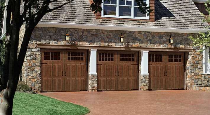 Three Amarr Classica Garage Door Carriage House Garage Doors in woodtone installed on a house.