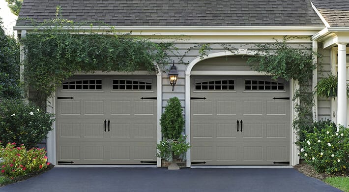 Two brown Amarr Heritage garage doors installed on a house with surrounding vines.